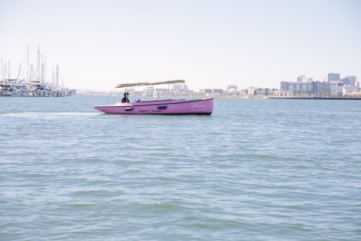The pink Fantail open-air electric boat on the water in Alameda