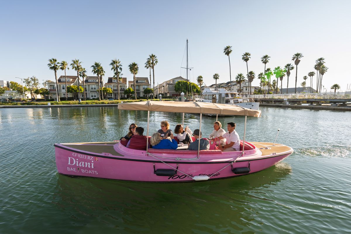 Guests aboard the pink Fantail electric boat cruising the calm water of the Oakland Estuary in Alameda